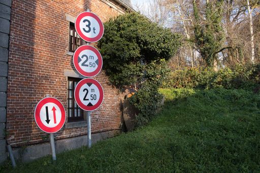 Poles of different road signs showing distance leaning against a building in a grass field