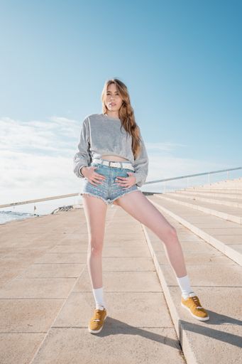 A vertical shot of a young blonde Caucasian woman wearing shorts and posing on the stairs