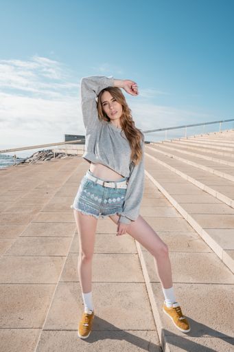A vertical shot of a young blonde Caucasian woman wearing shorts and posing on the stairs
