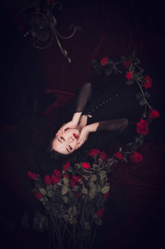 A vertical shot of an East Asian girl with black dress lying on her back with her hands on her face