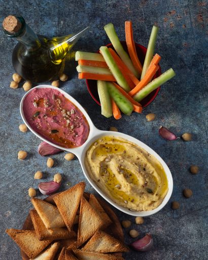 A vertical top view of an appetizing chickpea and beetroot hummus served with sliced carrot and cucumber