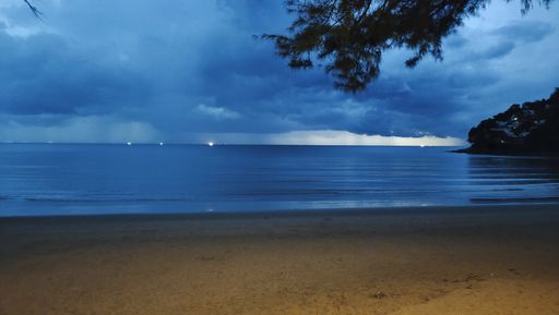 A beach surrounded by the sea and greenery under a cloudy sky during the evening
