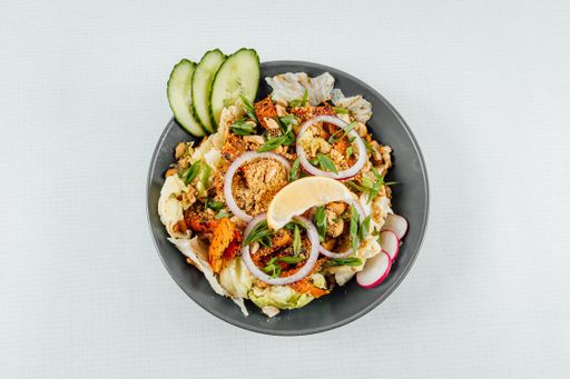 A to view closeup of roasted orange bell peppers, onion, radish, lemon and lettuce in a black bowl