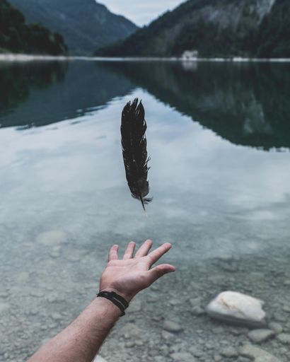 A black feather floating above an open palm of a man on a beautiful natural background