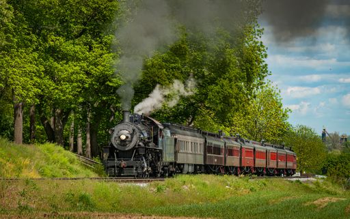 View of an Antique Restored Steam Passenger Train Approaching Along a Lone Rail Road Track on a Spring Day