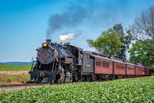View of an Antique Restored Steam Passenger Train Approaching Along a Lone Rail Road Track Traveling Thru the Countryside on a Spring Day