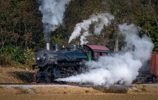 Ronks, Pennsylvania, November 8, 2021 - A View of a Restored Steam Freight Train Blowing Smoke and Steam Traveling Along a Rural Countryside
