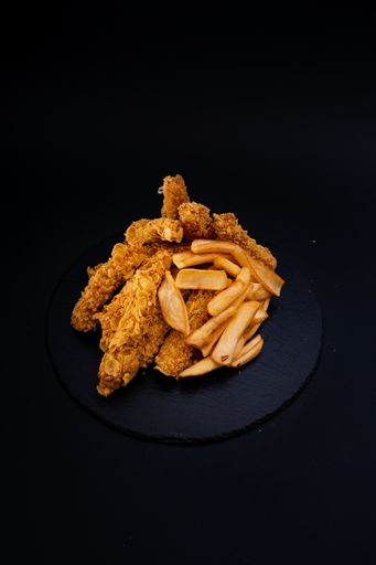 A closeup shot of a tasty looking dish with fried chicken and fries isolated on a black background