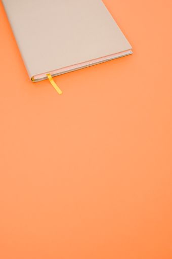 A top view closeup of a grey notebook with a yellow bookmark isolated on an orange background