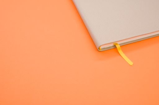 A top view closeup of a grey notebook with a yellow bookmark isolated on an orange background