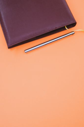 A top view closeup of a black notebook with a yellow bookmark and a pen isolated on an orange background