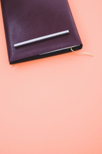 A top view closeup of a black notebook with a yellow bookmark and a pen isolated on an orange background