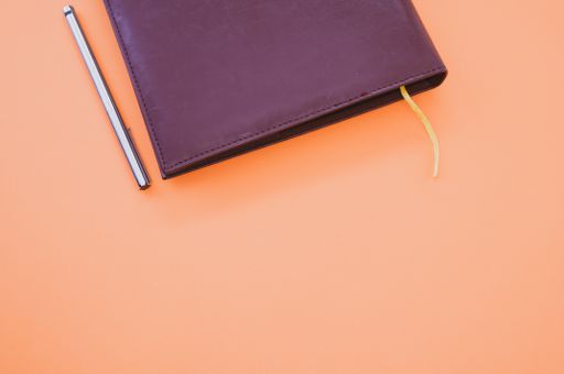 A top view closeup of a black notebook with a yellow bookmark and a pen isolated on an orange background
