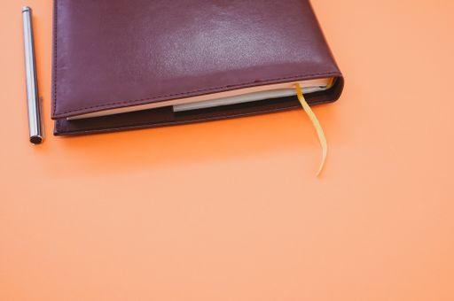 A top view closeup of a black notebook with a yellow bookmark and a pen isolated on an orange background