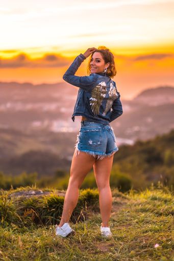A vertical shot of a Caucasian woman wearing jeans shorts and a jacket with angel wings during the sunset