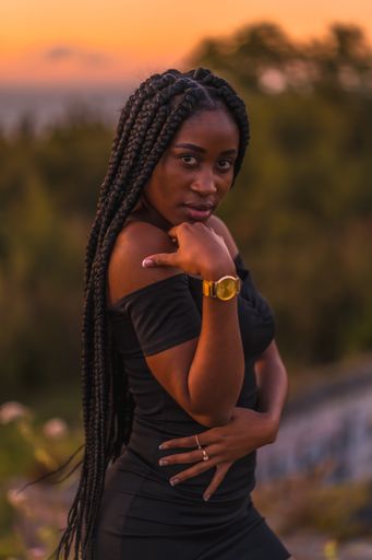 A vertical shot of an African-American woman with long braids posing during the sunset