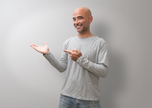 A Hispanic bald man smiling and showing right by his hands on a gray background