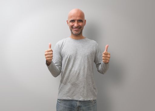 A Hispanic bald man smiling and showing his thumbs on a gray background