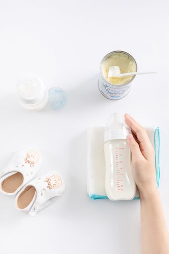 A vertical top view of a female hand and baby care items on a white surface