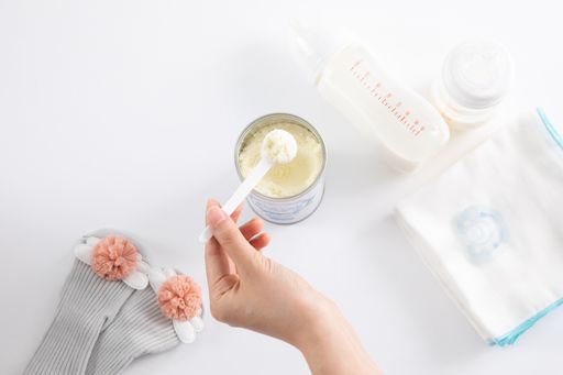 A top view of a female hand and baby care items on a white surface