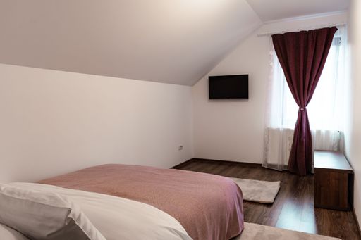 A cozy bedroom interior with little furniture and a TV on the wall