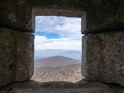 A closeup shot of an ancient stone-made building window opening with a beautiful nature view
