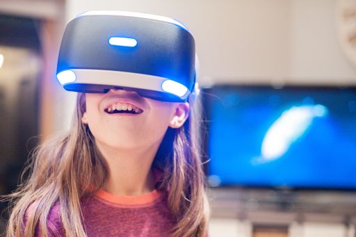 A closeup shot of a happy little smiling girl living through unbelievable emotions with VR glasses