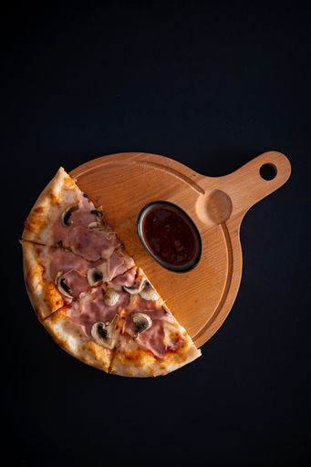 A top view of a freshly baked cheesy pizza with ham, mushrooms, and sauce on a wooden tray