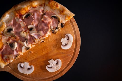 A top view of a freshly baked cheesy pizza  with ham and mushrooms on a wooden tray