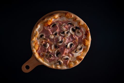 A top view of a freshly baked cheesy pizza with ham and mushrooms on a wooden tray