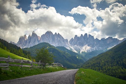 A narrow road surrounded by high green mountains leading to huge rocky cliffs