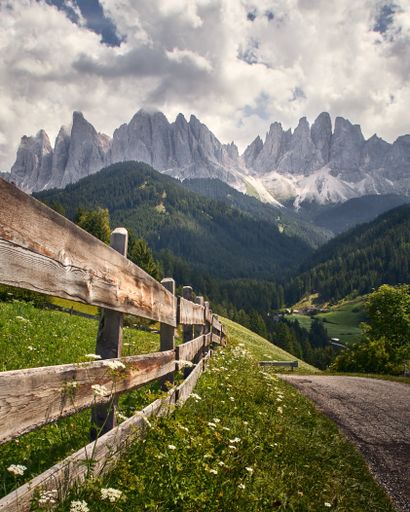 A vertical shot of a wooden fence with high rocky cliffs in the background in Funes Valley, St. Italy