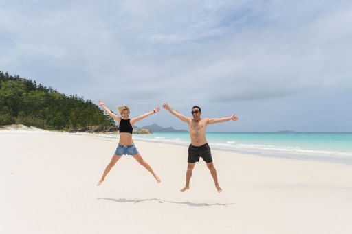 young happy couple jumping and laughing on the beach at whitehaven beach in Australia
