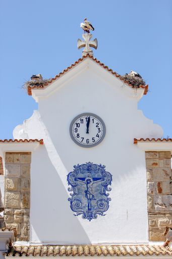 A vertical shot of a church with storks on the roof and  the cross