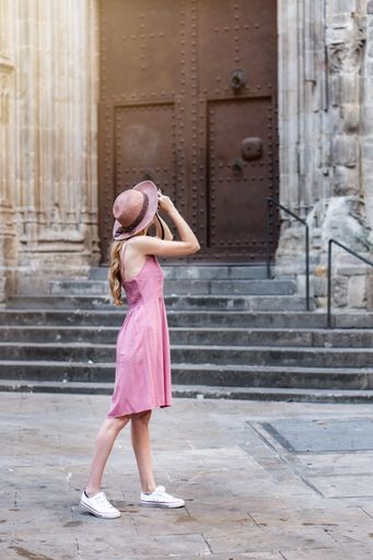 A vertical shot of a Caucasian blonde pretty tourist wearing a hat taking photos of the city