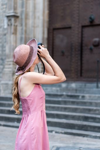 A vertical shot of a Caucasian blonde pretty tourist wearing a hat taking photos of the city