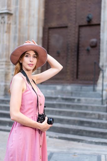 A vertical shot of a Caucasian blonde pretty tourist wearing a hat taking photos of the city