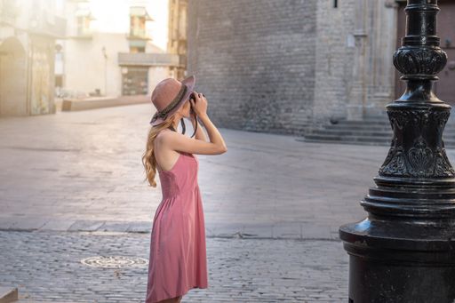 A Caucasian blonde pretty tourist wearing a hat taking photos of the city