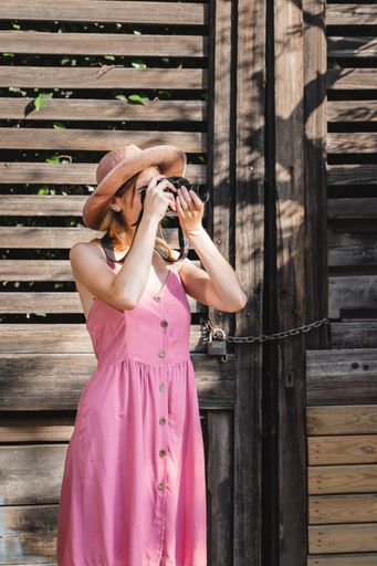 A vertical shot of a Caucasian blonde pretty tourist wearing a hat taking photos of the city