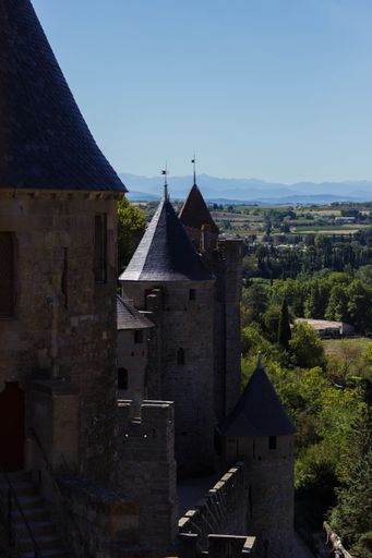 An old castle surrounded by greenery with rocky mountains on the background under sunlight