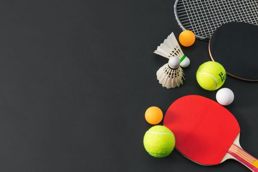 A high angle shot of ping pong balls and racketson a black surface