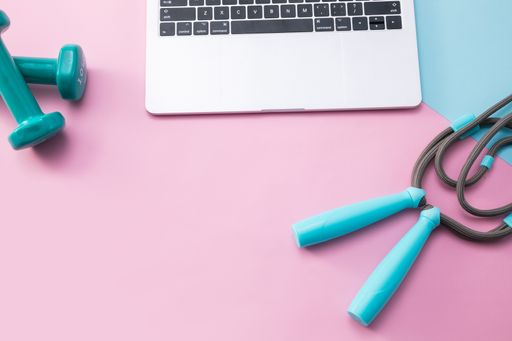 A top view shot of dumbbells, jump rope and a laptop on a mat