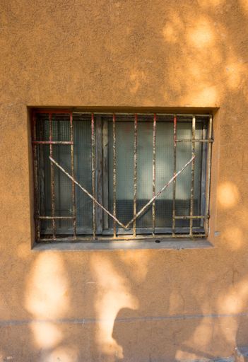 A closeup of a rusty metallic fence on the tiny window on an orange wall