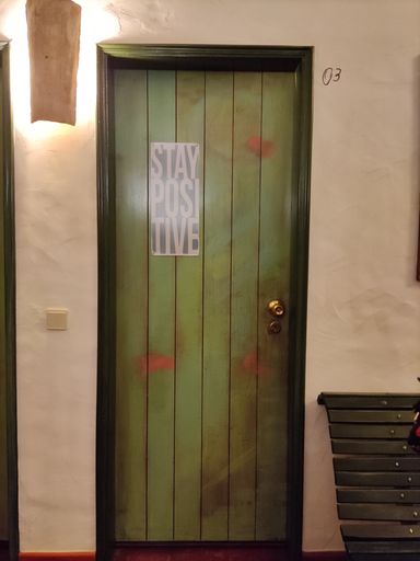 A vertical closeup fo a green wooden door with the text "stay positive" on it