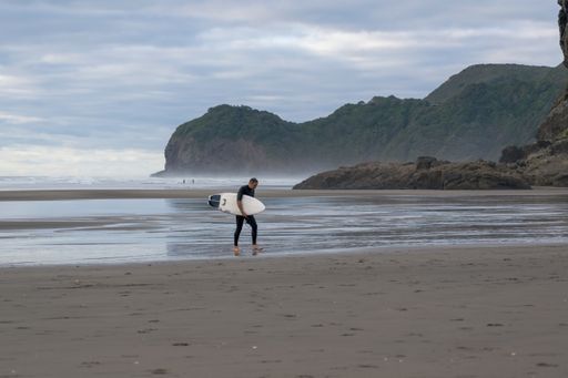 Auckland / New Zealand - February 11 2020: View of tired surfer walking on Piha beach
