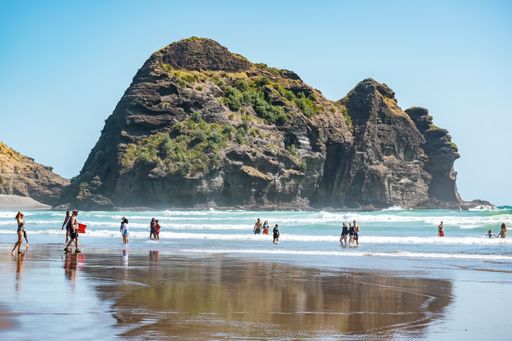 Auckland / New Zealand - January 31 2020: View of people having fun at Piha beach with Camel Rock cliff face ocean in background
