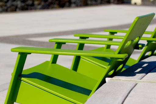 Three green chairs situated side by side on a concrete path on a sunny day