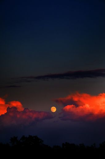 A vertical shot of the moon and fire clouds in the dark sky