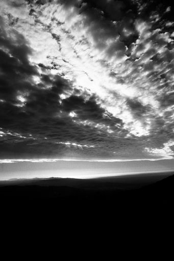A vertical greyscale shot of the sun shining behind storm clouds