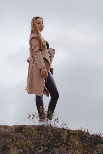 A vertical shot of a young blonde Caucasian woman standing on the top of the hill during a cloudy day
